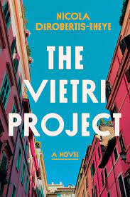 Book cover for Nicola DeRobertis-Theye book The Vietri Project, showing view on an Italian street looking up at buildings with the sky above, title in white capital letters with the words A Novel in yellow-orange capital letters below that followed by the author's name at the bottom, all three lines of text centered on cover