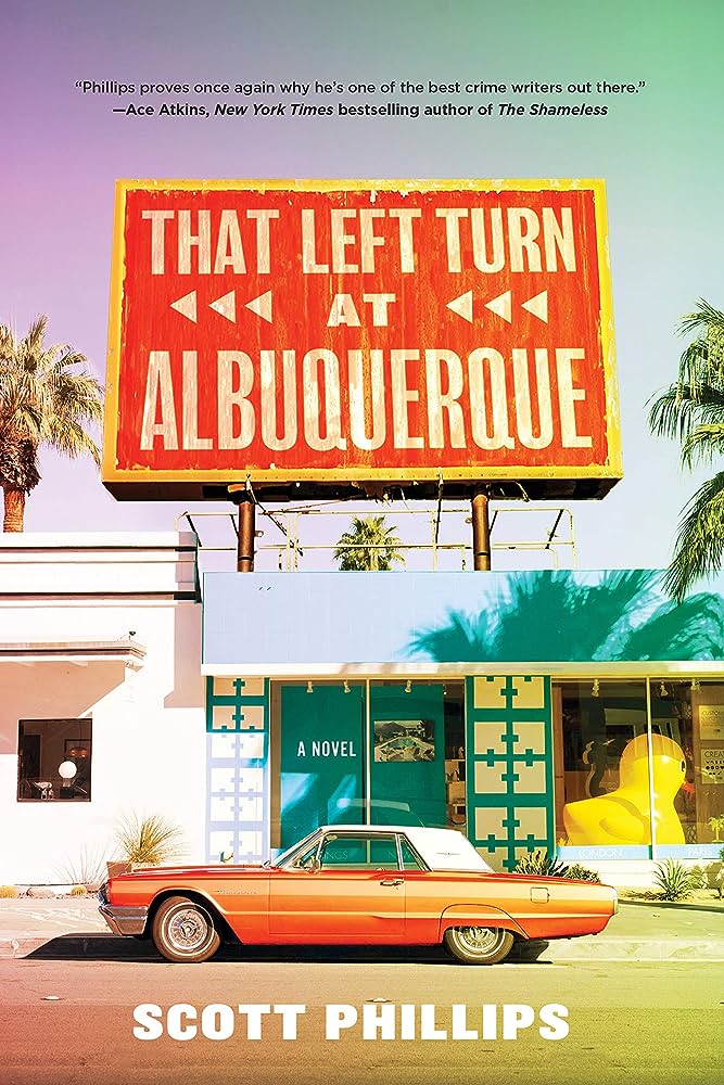 Book cover for That Left Turn at Albuquerque by Scott Phillips photograph of large billboard with the writing "that left turn at Albuquerque" on the roof of a one-story building that looks like a shop with a giant yellow rubber duck in the window with an old American car parked in front