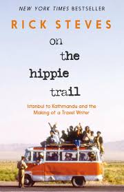 Book cover for On the Hippie Trail: Istanbul to Kathmandu and the Making of a Travel Writer, by Rick Steves color photograph showing a small orange and white bus traveling from right to left, stopped, with an official in a brown uniform looking at or writing something. The bus is packed with passengers inside and also on top of the roof, hanging on. In the background there is some short scrub grass, yellowish-green, with low brown mountains in the far distance