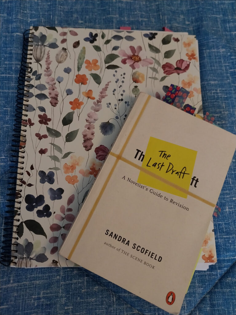 Color photo of Sandra Scofield's book The Last Draft: A Novelist's Guide to Revision on to of a Miquelrius notebook with a brightly-colored flower design on the cover