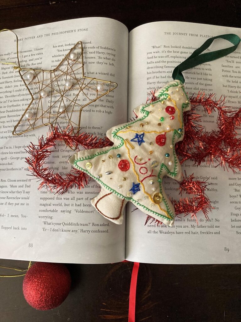 Image of Christmas tree ornament shaped like a white Christmas tree on top of an open book with other Christmas decorations around it